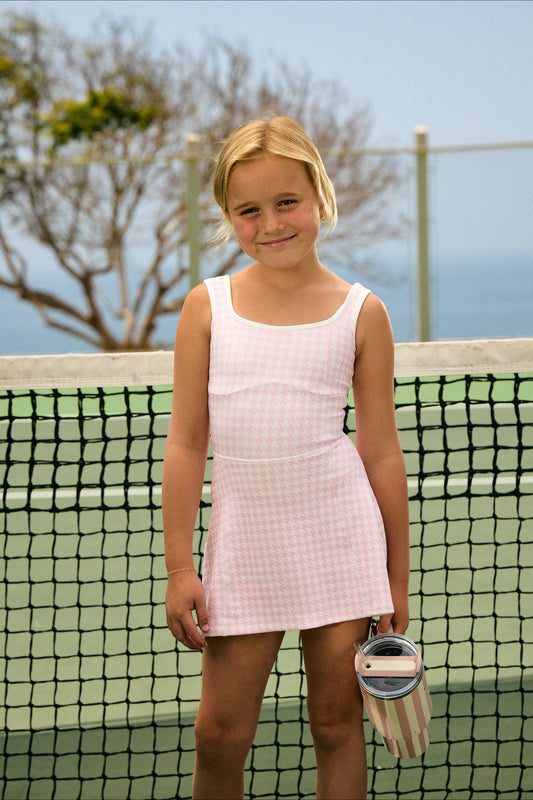 Mini Morgan Dress – girls' pink houndstooth tennis dress, on court at the net :: Gemma is 8 and wears a size 7-8